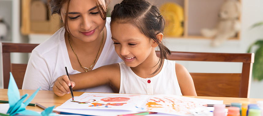Young girl painting something colourful while her mother looks on