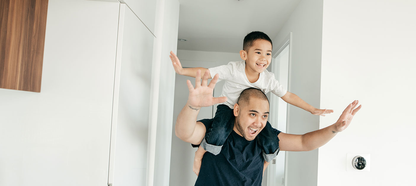 A young boy sits piggyback on his father’s shoulders as they tour their new home