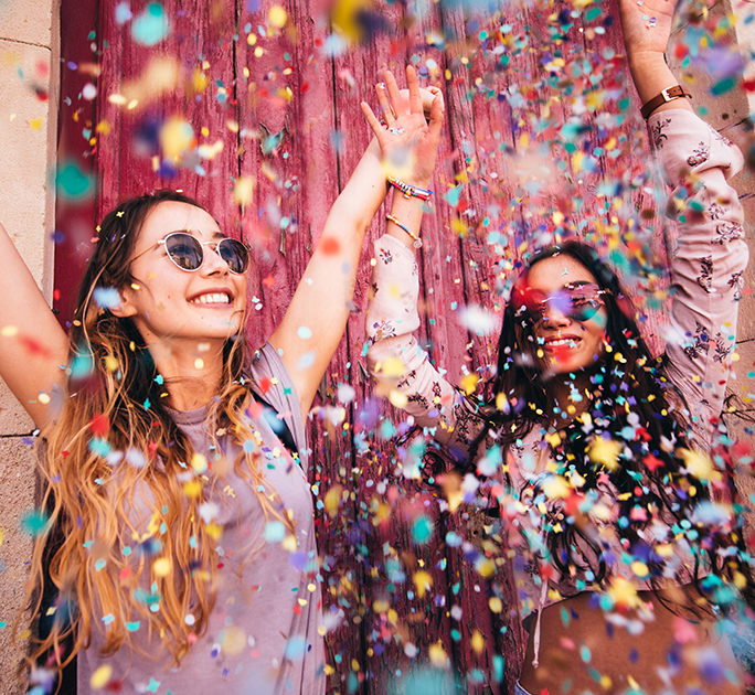 Two young women enjoying themselves at a music festival, surrounded by colourful confetti thrown in the air