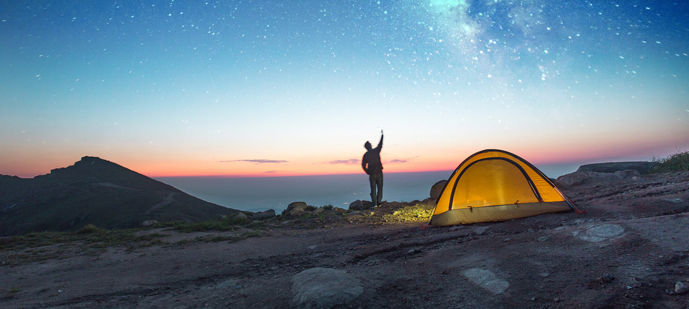 Solo camper in the great outdoors, taking a selfie against a star-lit dusk sky